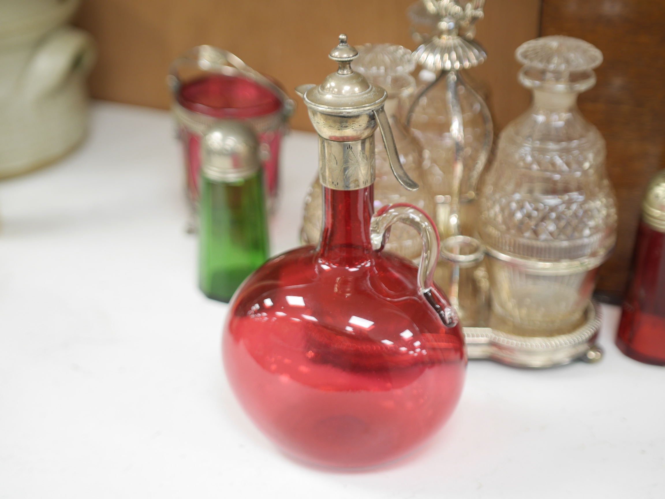 A cased silver plated three bottle liqueur stand, a cranberry decanter, sugar shaker and jam stand together with a green glass shaker, stand 27cm high (5). Condition - all items in good condition, box in need of a clean